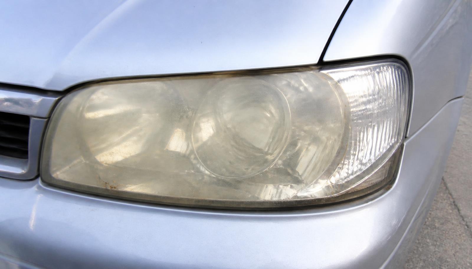 Severely yellowed and oxidized headlight lens on a silver sedan compared to the clear paint beside it