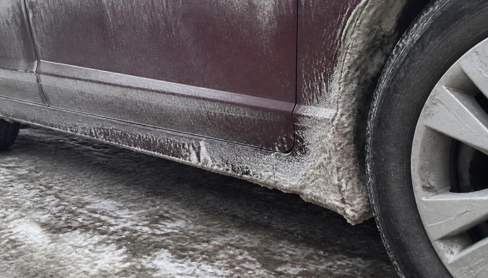 Thick white road salt residue crusted on the rocker panel and wheel well of a car during a Minnesota winter